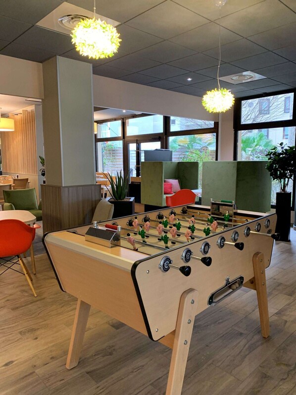 Un espace intérieur moderne doté d’un baby-foot, de coins salon et de grandes fenêtres laissant entrer la lumière naturelle.