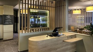 A reception desk with a wooden counter, a wine display behind a wooden partition, and a seating area with tables and chairs. - ibis Tours Centre Gare (Tours)