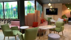 A modern lounge area with green and pink seating, round tables, and a large TV screen. - ibis Tours Centre Gare (Tours)