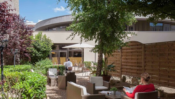 An outdoor patio with wicker furniture, a waiter, and a building in the background. - ibis Tours Centre Gare (Tours)
