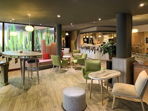 A modern interior with round tables, green chairs, a bar area, and a cactus-themed wall. - ibis Tours Centre Gare (Tours)