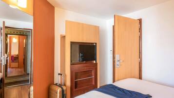 A hotel room with a bed, a television, a suitcase, and a mirror.