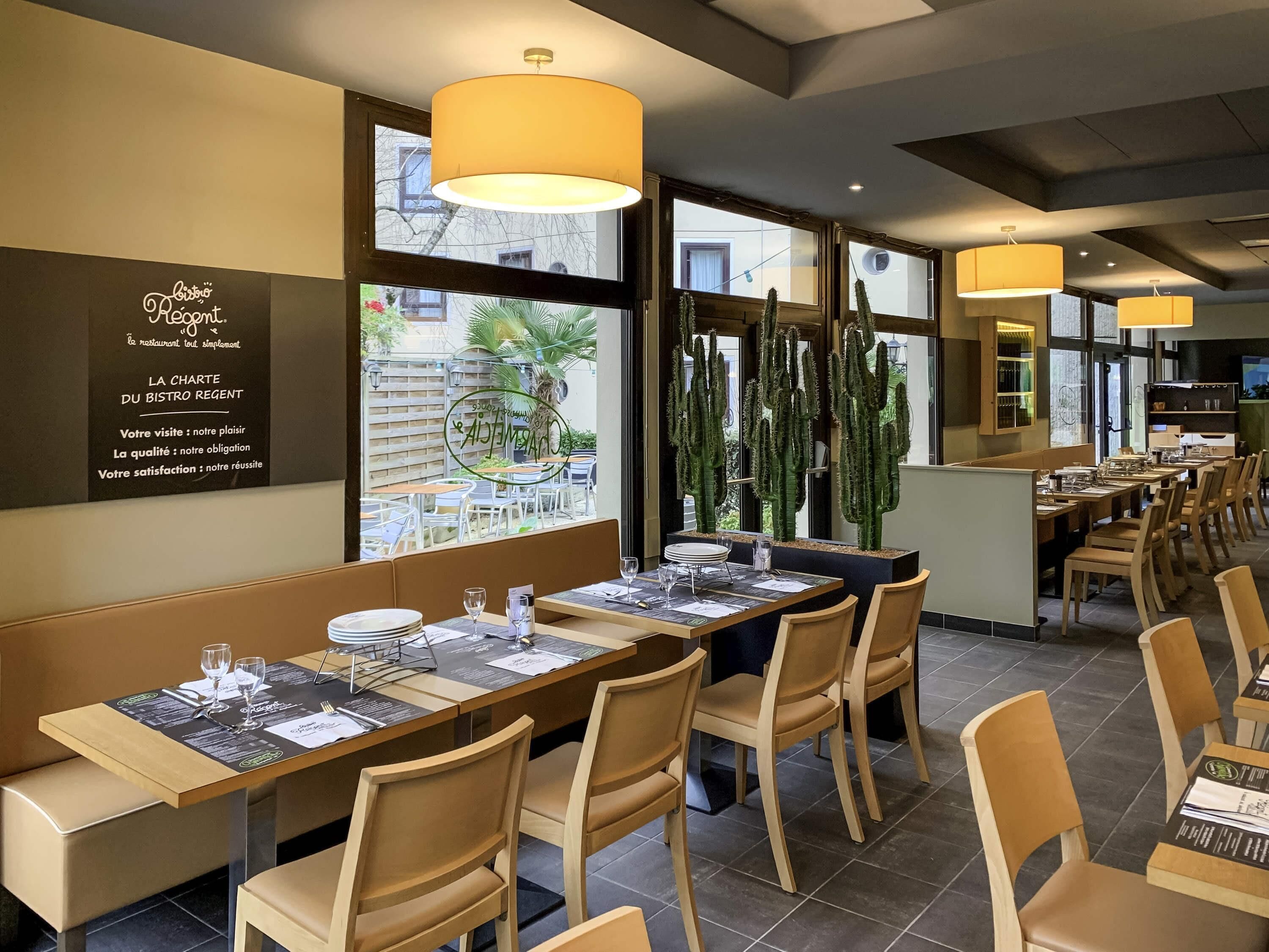 En restaurantindretning med lange borde, træstole og hængende lamper.