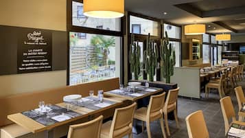 L’intérieur d’un restaurant avec de longues tables, des chaises en bois et des lampes suspendues.