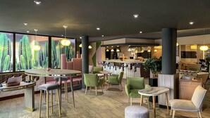 A modern lounge area with round tables, green and white chairs, and a bar area with a counter and stools. - ibis Tours Centre Gare (Tours)