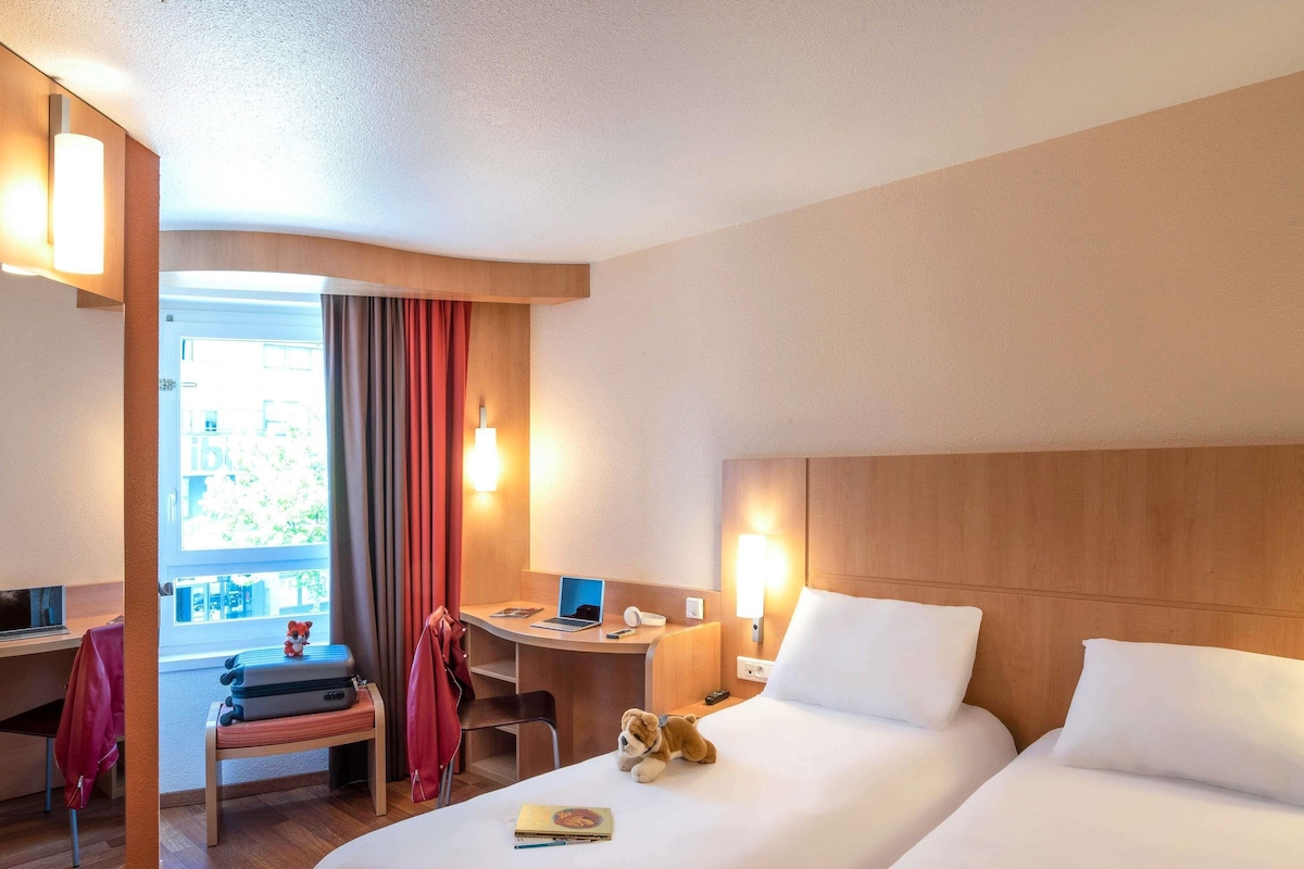 Habitación de hotel con dos camas, un escritorio, una silla, una computadora portátil y una ventana con cortinas.