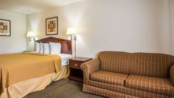 A hotel room with two beds, a sofa, and two wall-mounted lamps.
