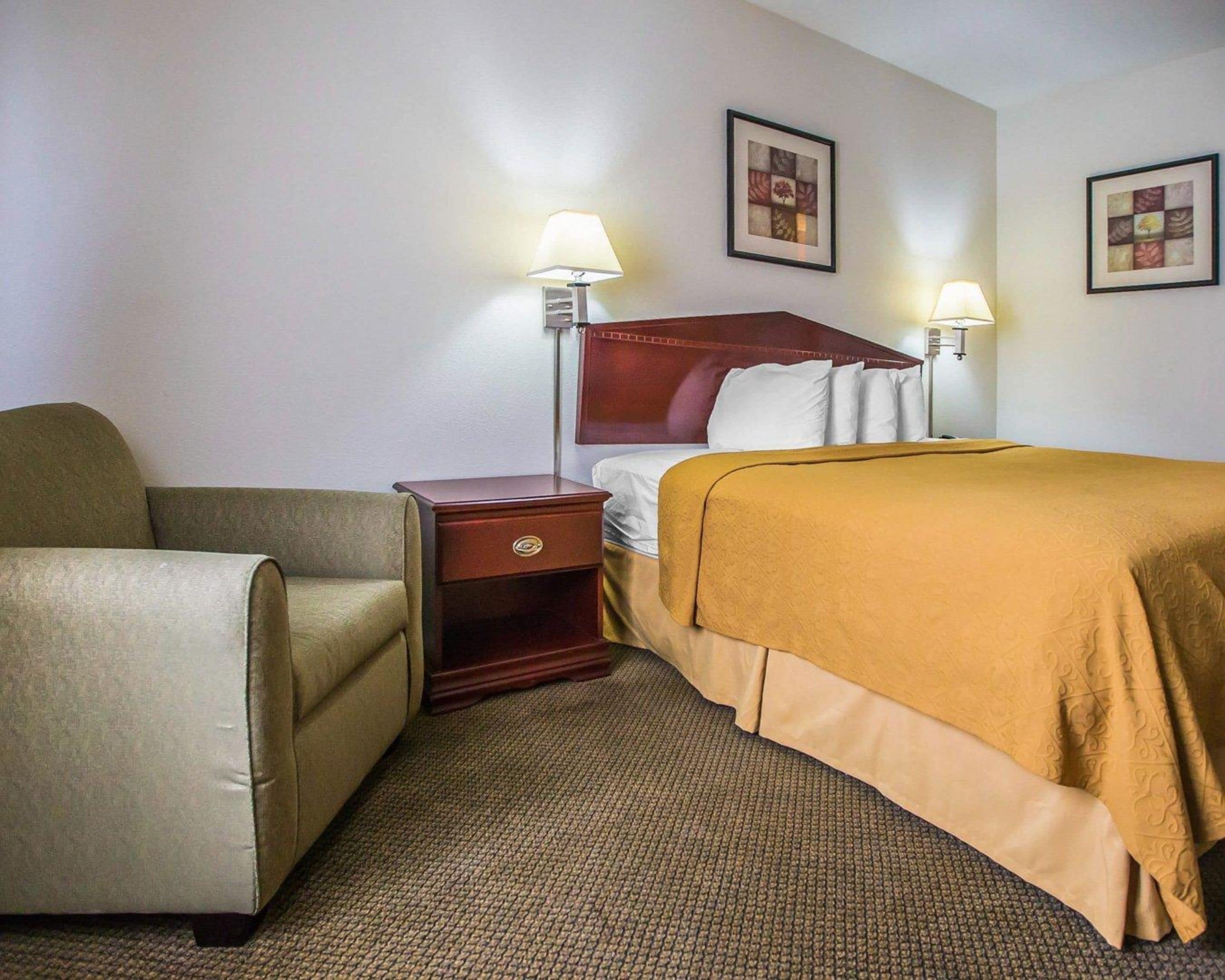 Una habitación de hotel con una cama individual, una mesita de noche, una silla y dos lámparas fijadas a la pared.