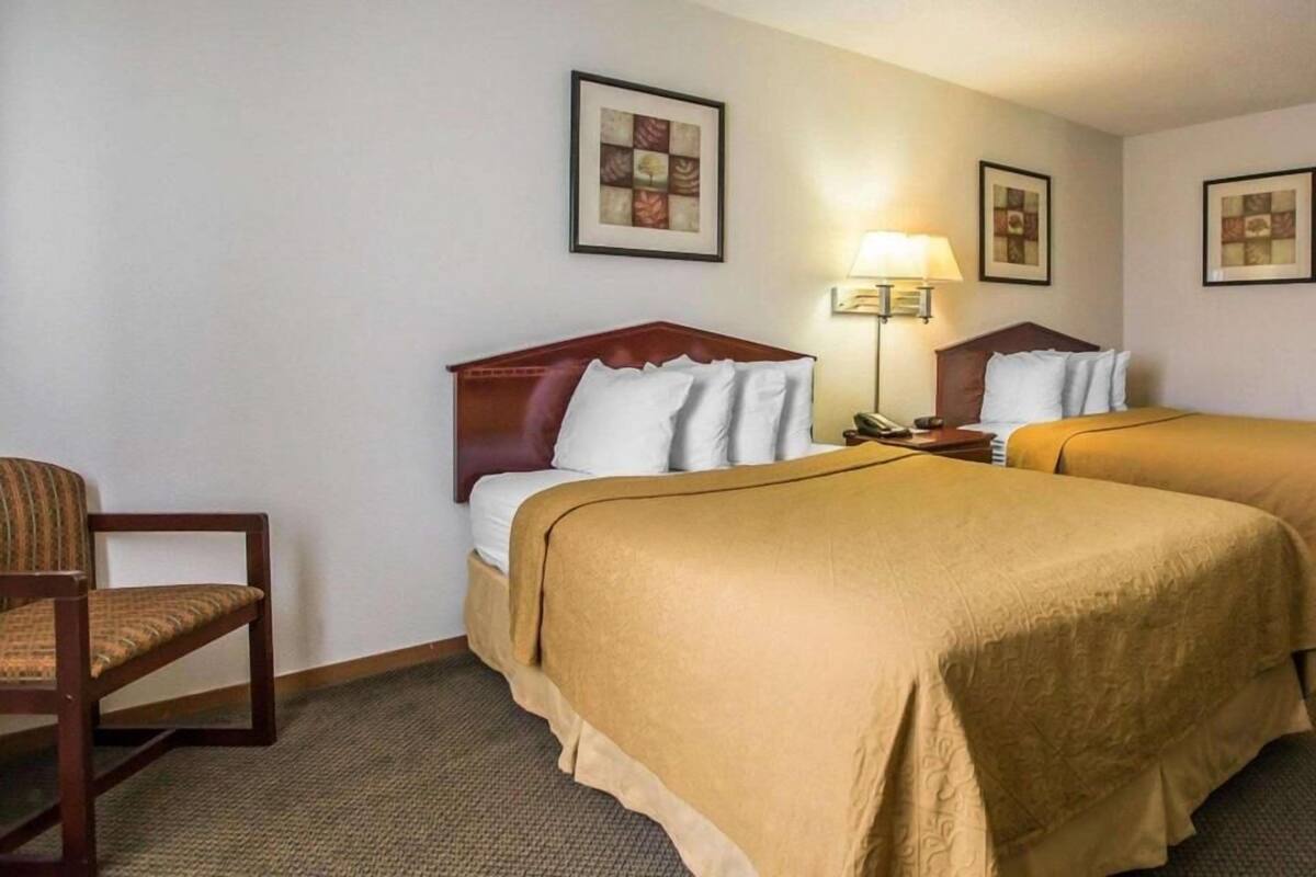 A hotel room with two beds, a chair, and a lamp.