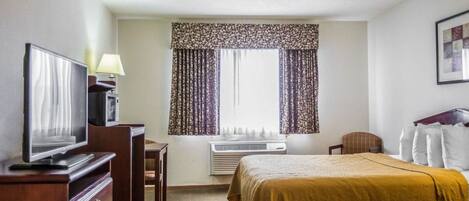 A hotel room with two beds, a desk with a television, a chair, and a window with curtains.