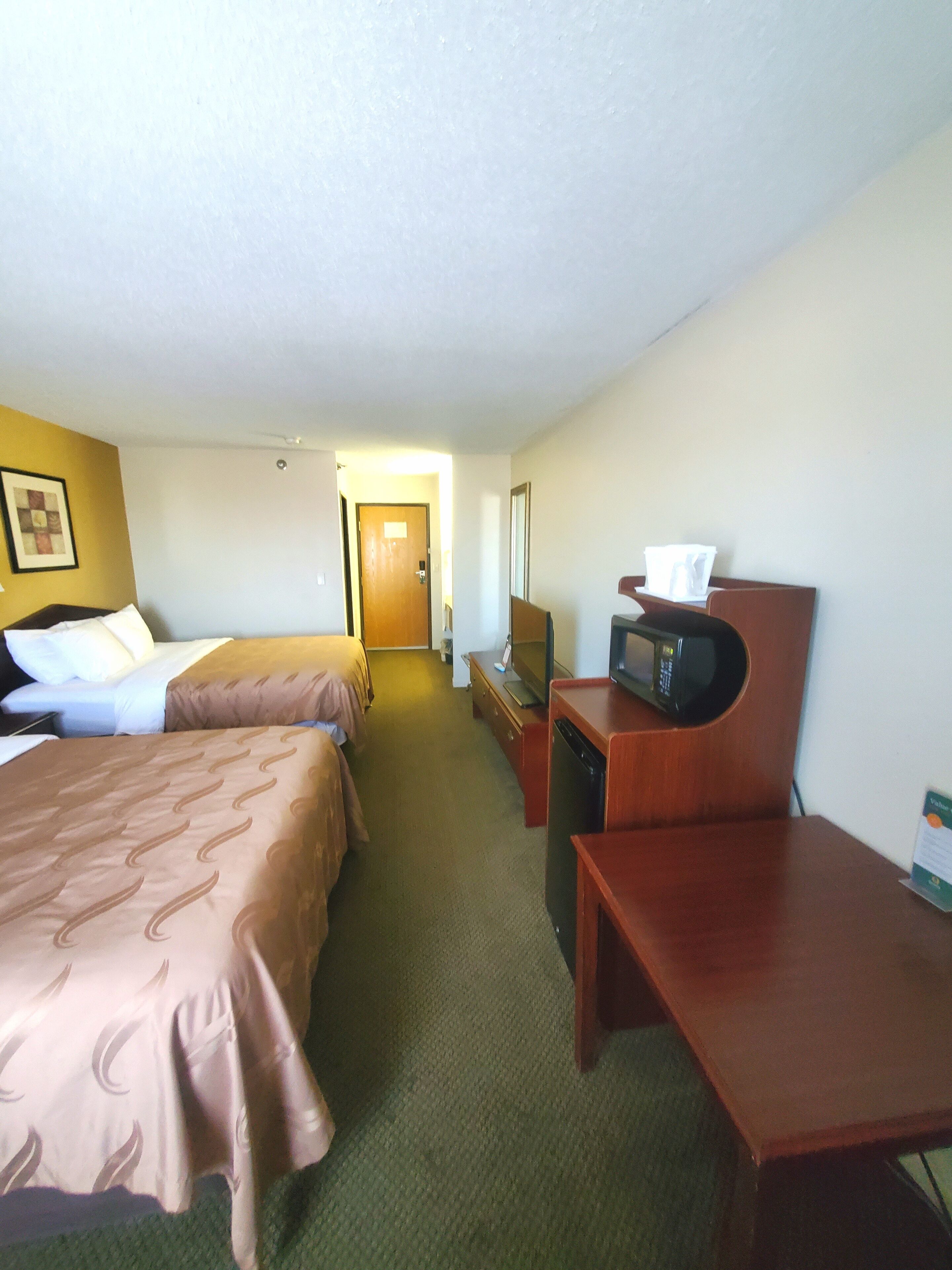 A hotel room with two beds, a desk, a television, and a microwave.