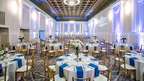 A banquet hall with round tables, blue tablecloths, and gold chairs.