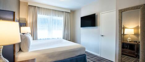 A hotel room with a bed, a TV mounted on the wall, a mirror, and a window with curtains.