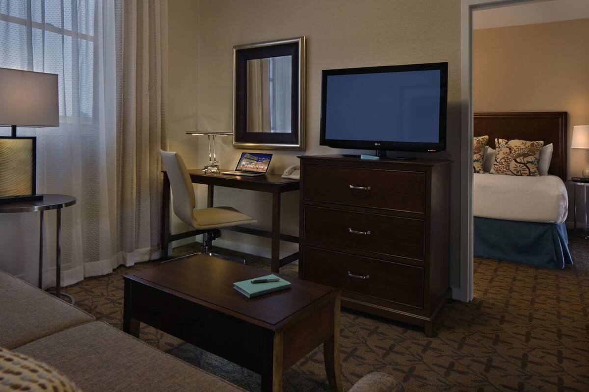 A hotel room with a desk, chair, television, dresser, and a bed.
