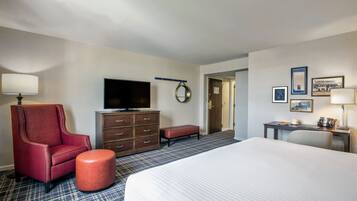 Una habitación de hotel con una cama grande, un sillón rojo, un aparador de madera, un televisor y un escritorio con lámpara.
