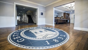 A hotel lobby with a circular emblem on the floor, a staircase, and a reception area.