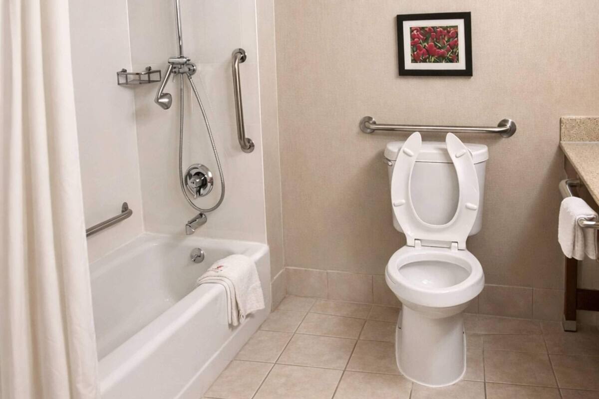 A bathroom with a bathtub, toilet, and shower. There is a handrail and a picture on the wall.