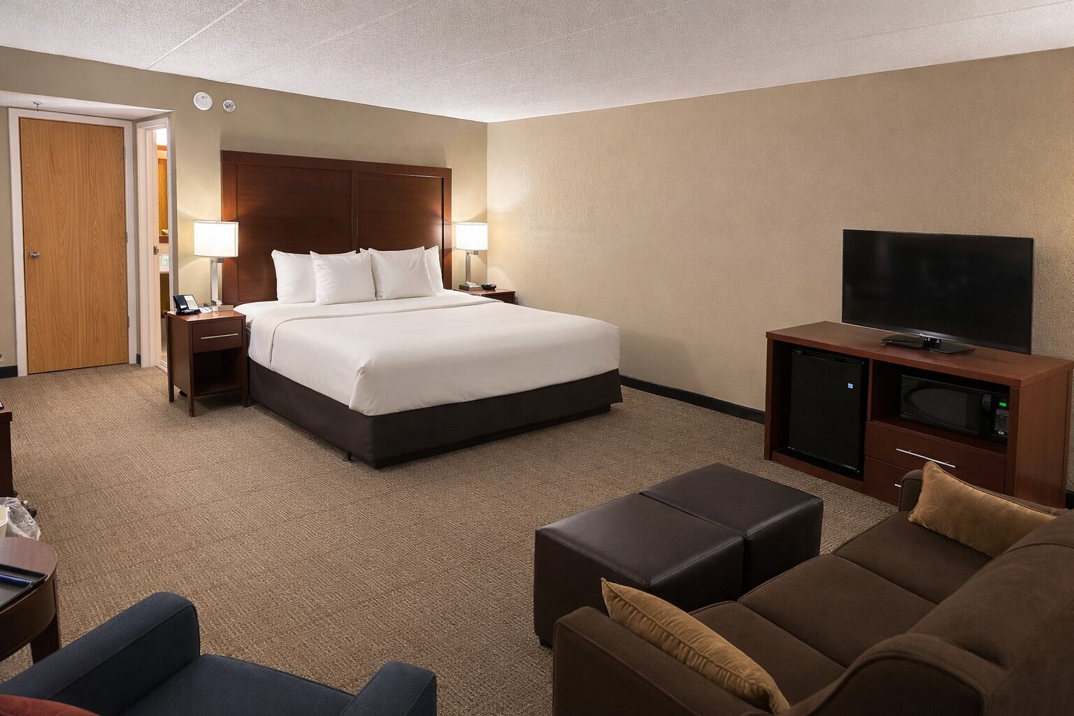 Una habitación de hotel con cama, mesitas de noche, televisor, sofá y una pequeña mesa.