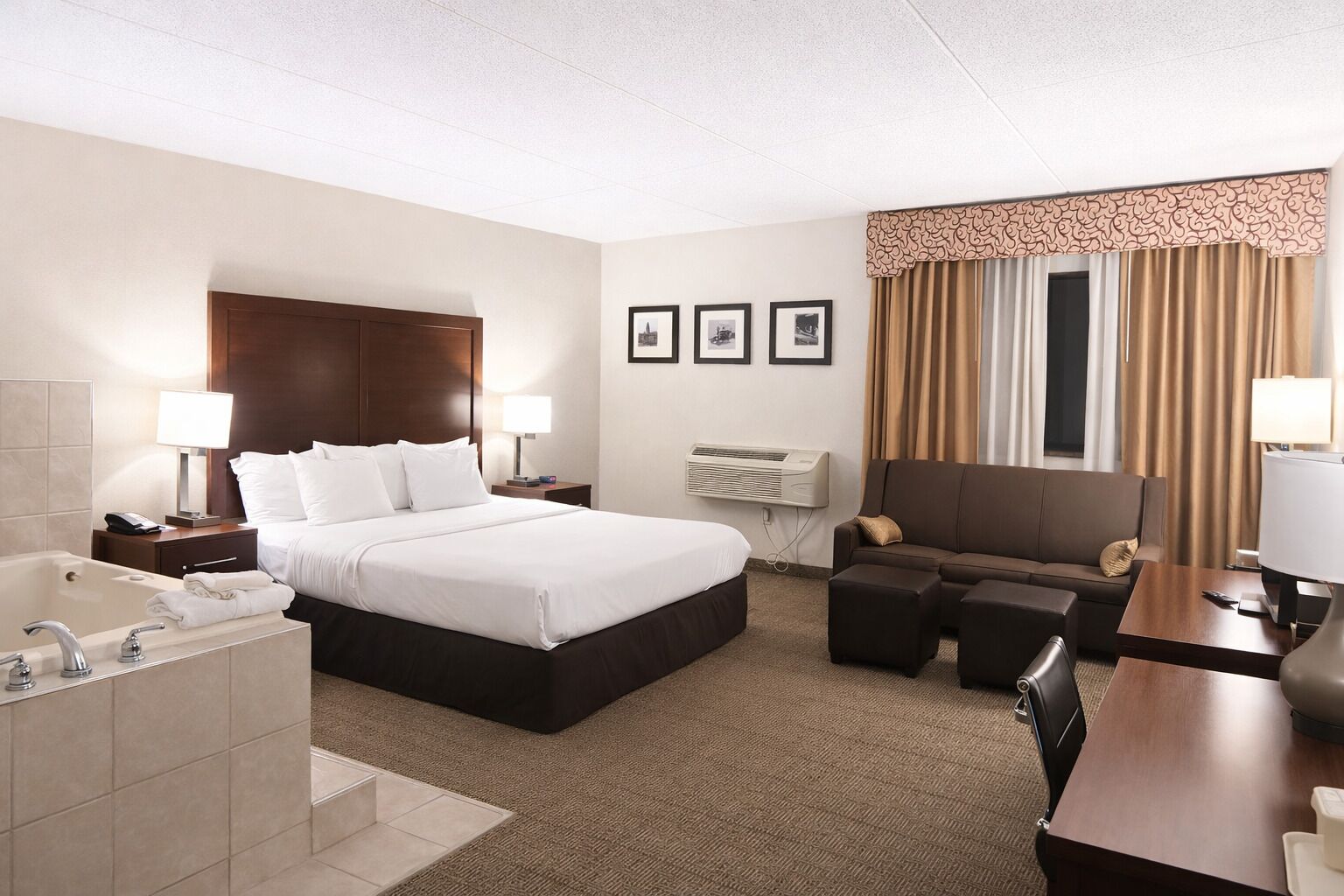 A hotel room with a large bed, a sitting area with a sofa and armchair, a desk, and a bathroom with a bathtub.