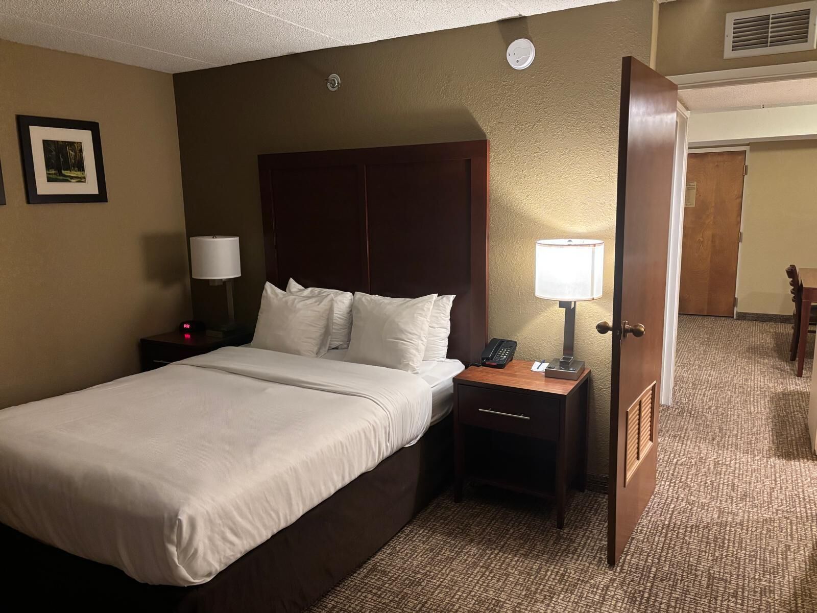 Une chambre d’hôtel avec un lit, des tables de chevet, une lampe, un téléphone et une porte.