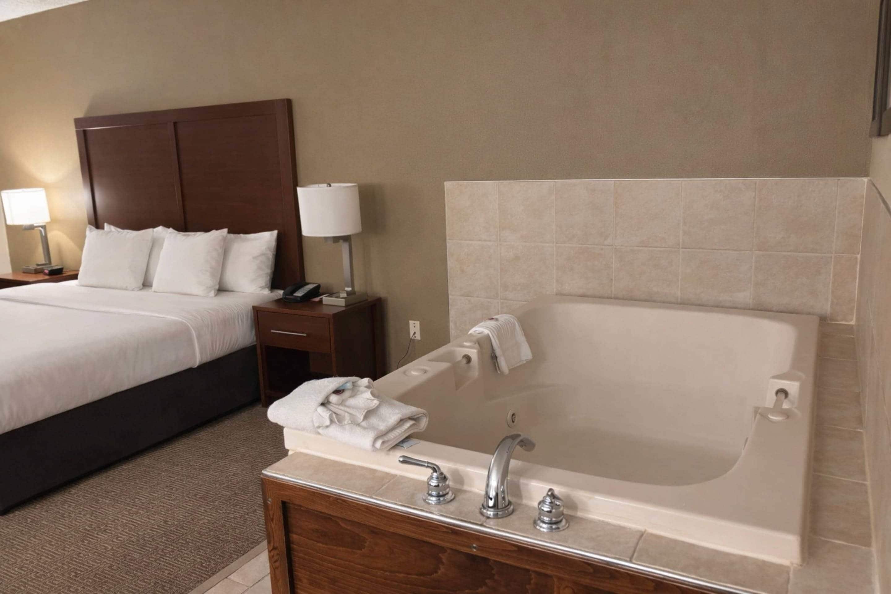 A hotel room with a large bed, a separate bathroom with a bathtub, and a wooden vanity.