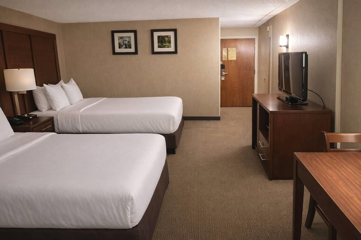 A hotel room with two beds, a desk, a television, and a door leading to a hallway.