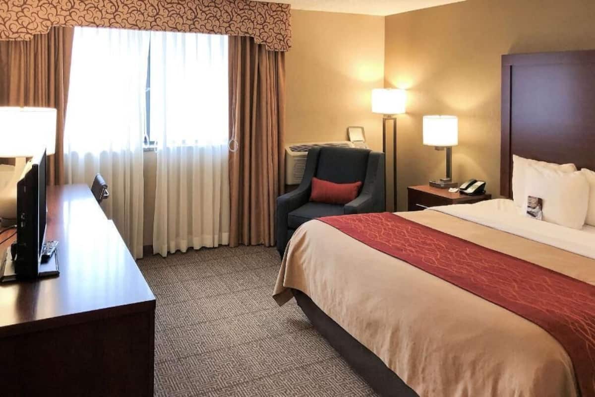 A hotel room with a bed, desk, chair, lamps, and a window with curtains.