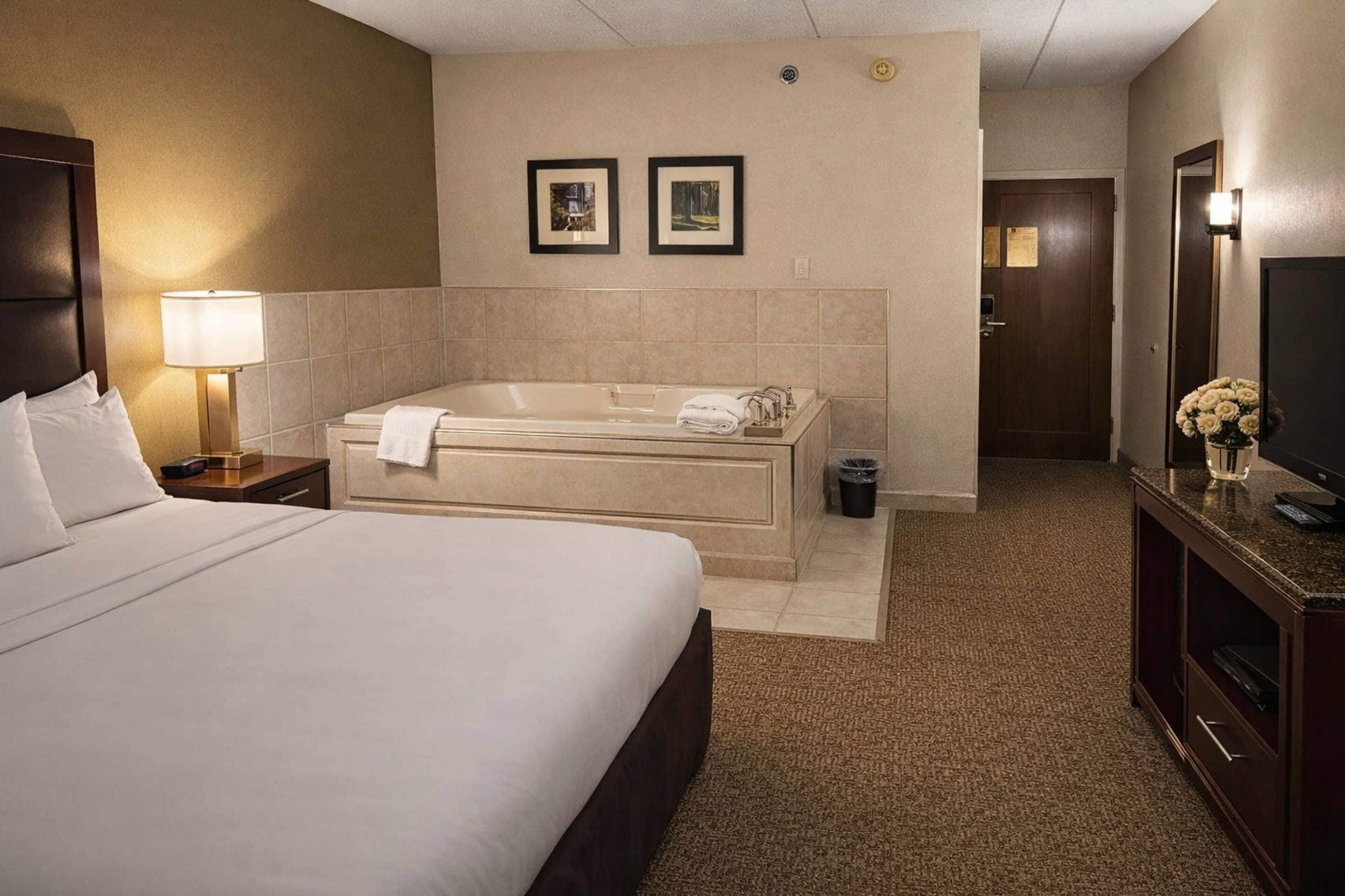 A hotel room with a large bed, a separate bathtub, a television, and a desk with a lamp.