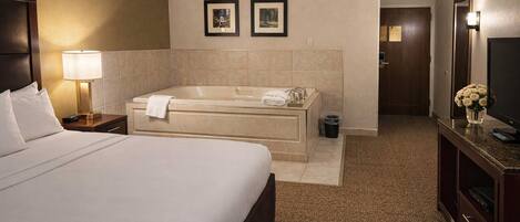 A hotel room with a large bed, a separate bathtub, a television, and a desk with a lamp.