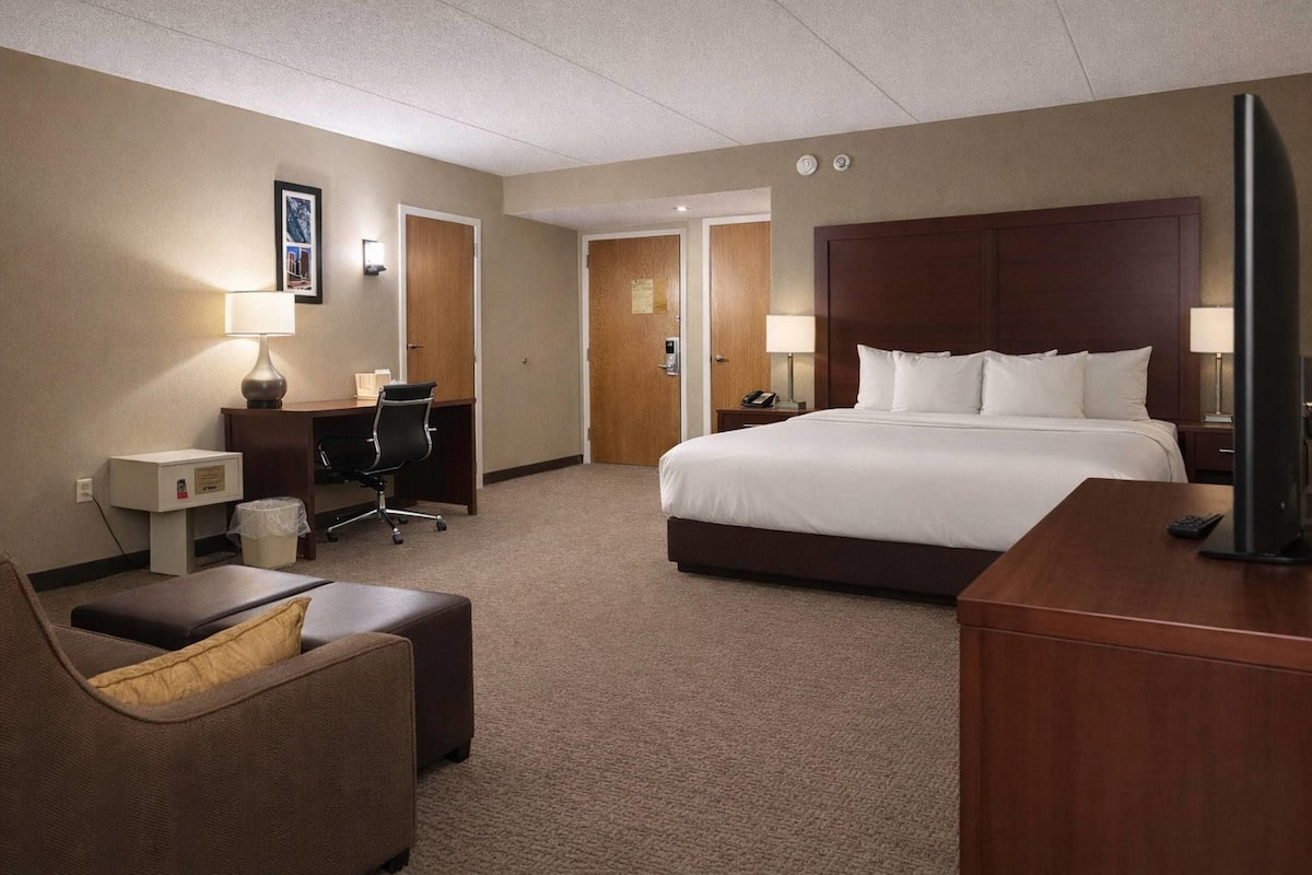 A hotel room with a large bed, a desk, a chair, and a television.