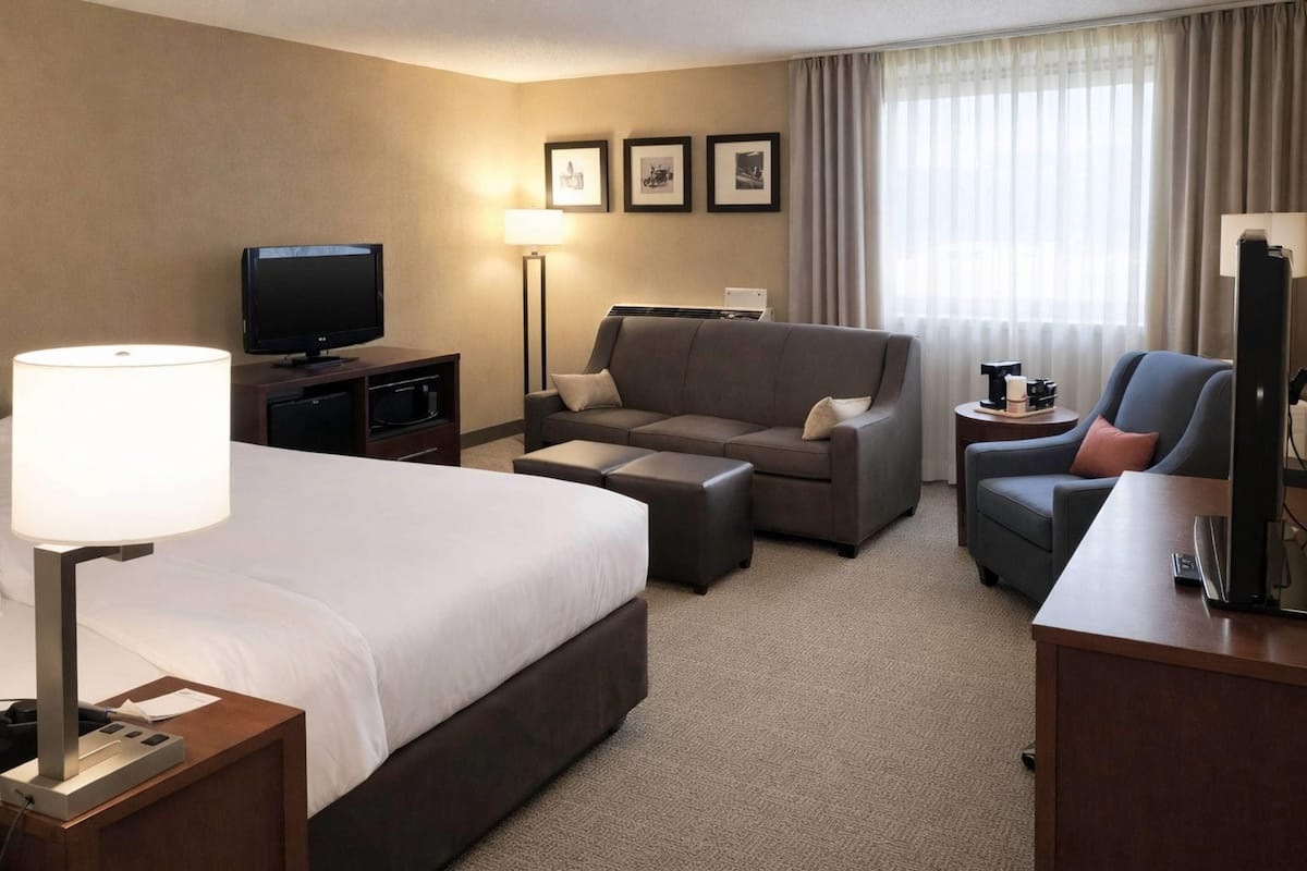 A hotel room with a bed, a sofa, a TV, a desk, and a lamp.