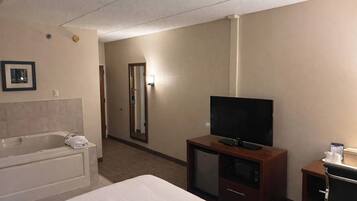 A hotel room with a bed, a TV, a small desk, a mirror, and a bathroom with a bathtub and toilet.