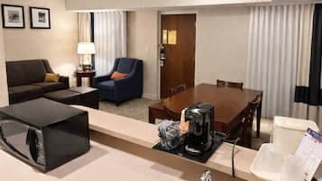 Habitación de hotel con una mesa de comedor, un sofá, una silla, microondas, cafetera, lavabo y una bandeja con jarra de café y vasos.
