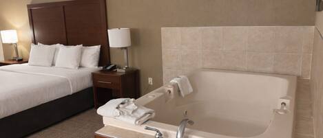 Une chambre d’hôtel comprenant un lit, une table de chevet avec une lampe, une salle de bain avec une baignoire et une coiffeuse en bois.
