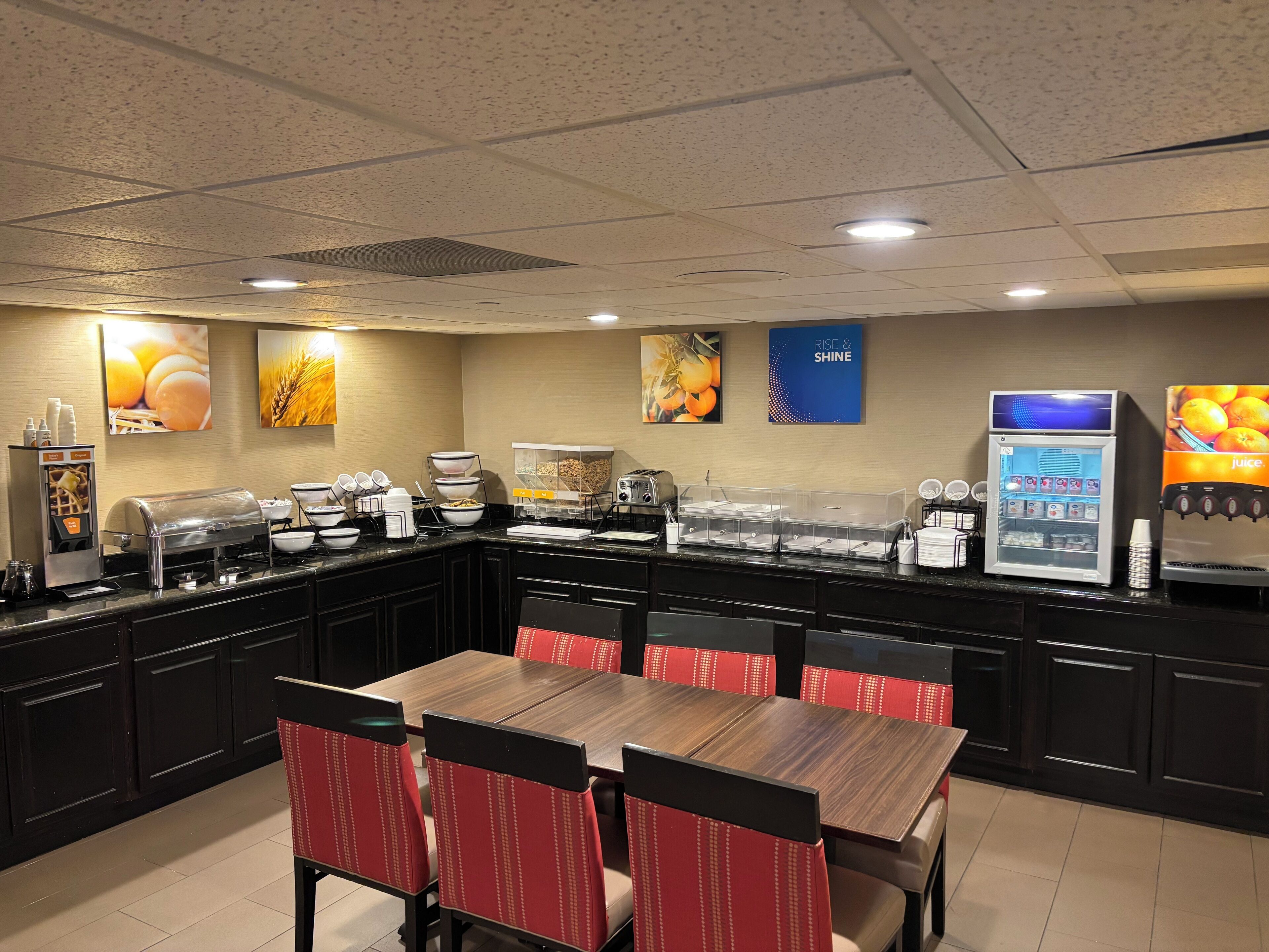 Un área de desayuno con servicio tipo buffet, que incluye una cafetera, dispensador de zumo y varios recipientes de comida.
