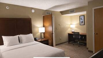 Une suite composée d’une chambre avec un lit, une table de chevet avec une lampe, un bureau avec une chaise et une porte.