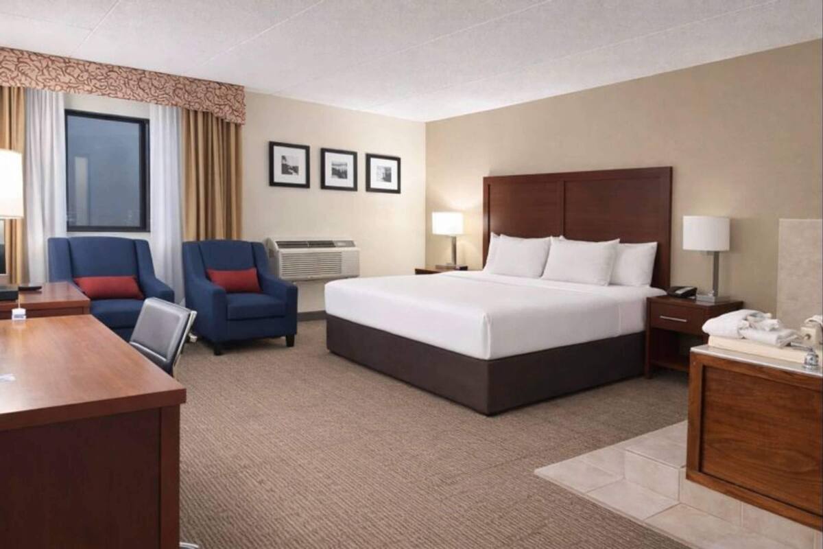A hotel room with a large bed, two armchairs, a desk, and a bedside table.