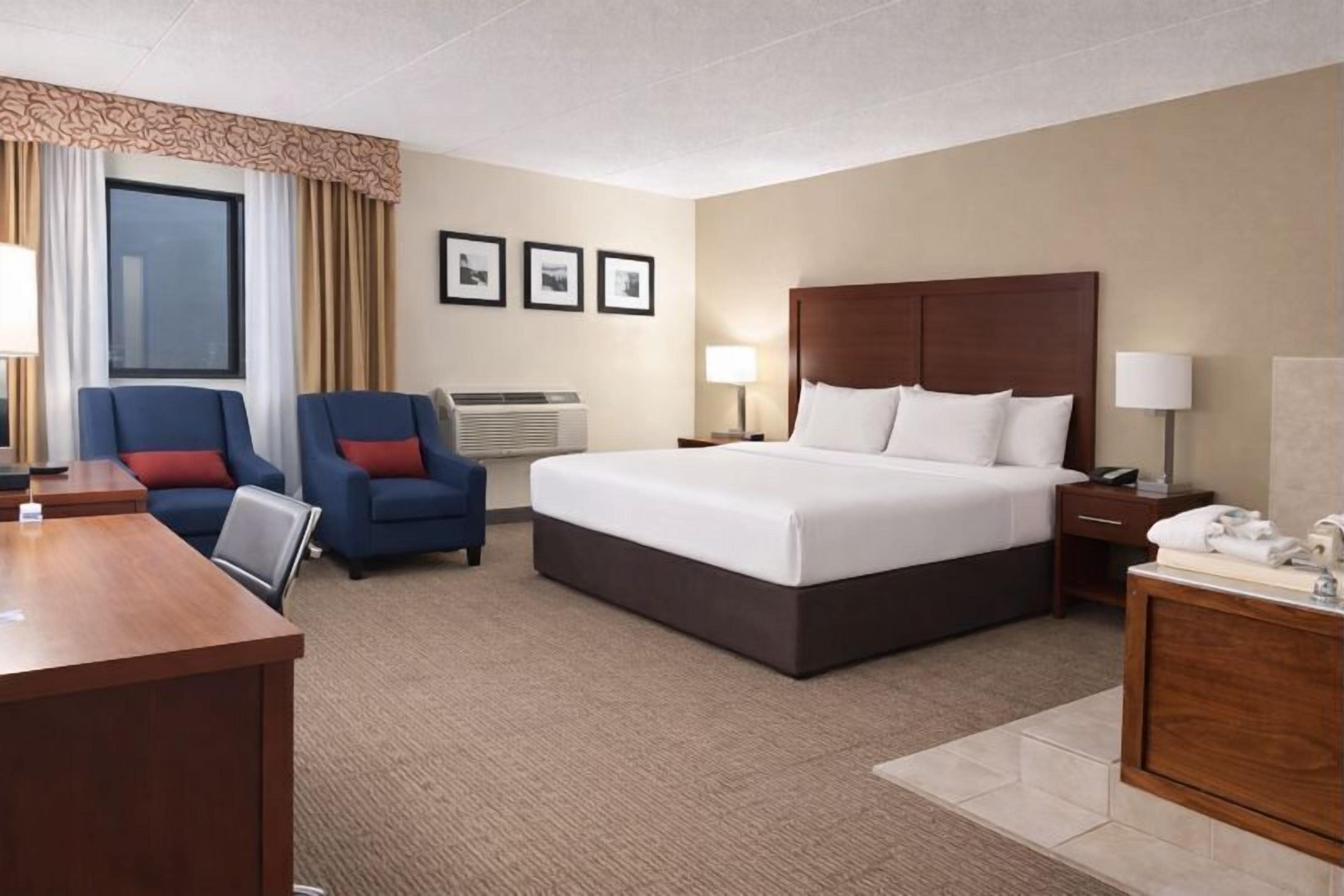 Une chambre d’hôtel avec un grand lit, deux fauteuils, un bureau et une petite salle de bain.