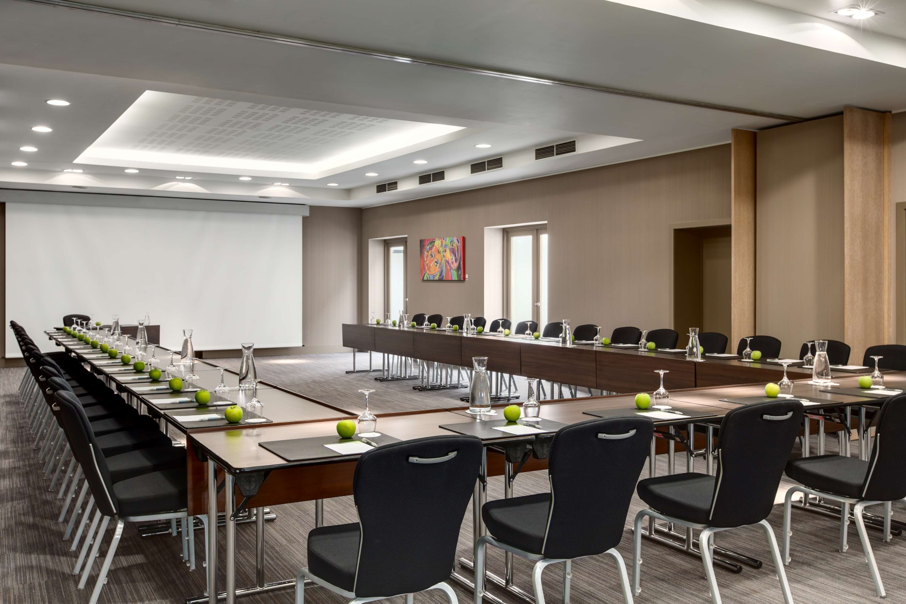 Une salle de conférence équipée de longues tables, de chaises et d’un écran de projection.