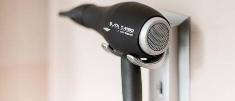 A black hairdryer mounted on a wall, connected to a power outlet.