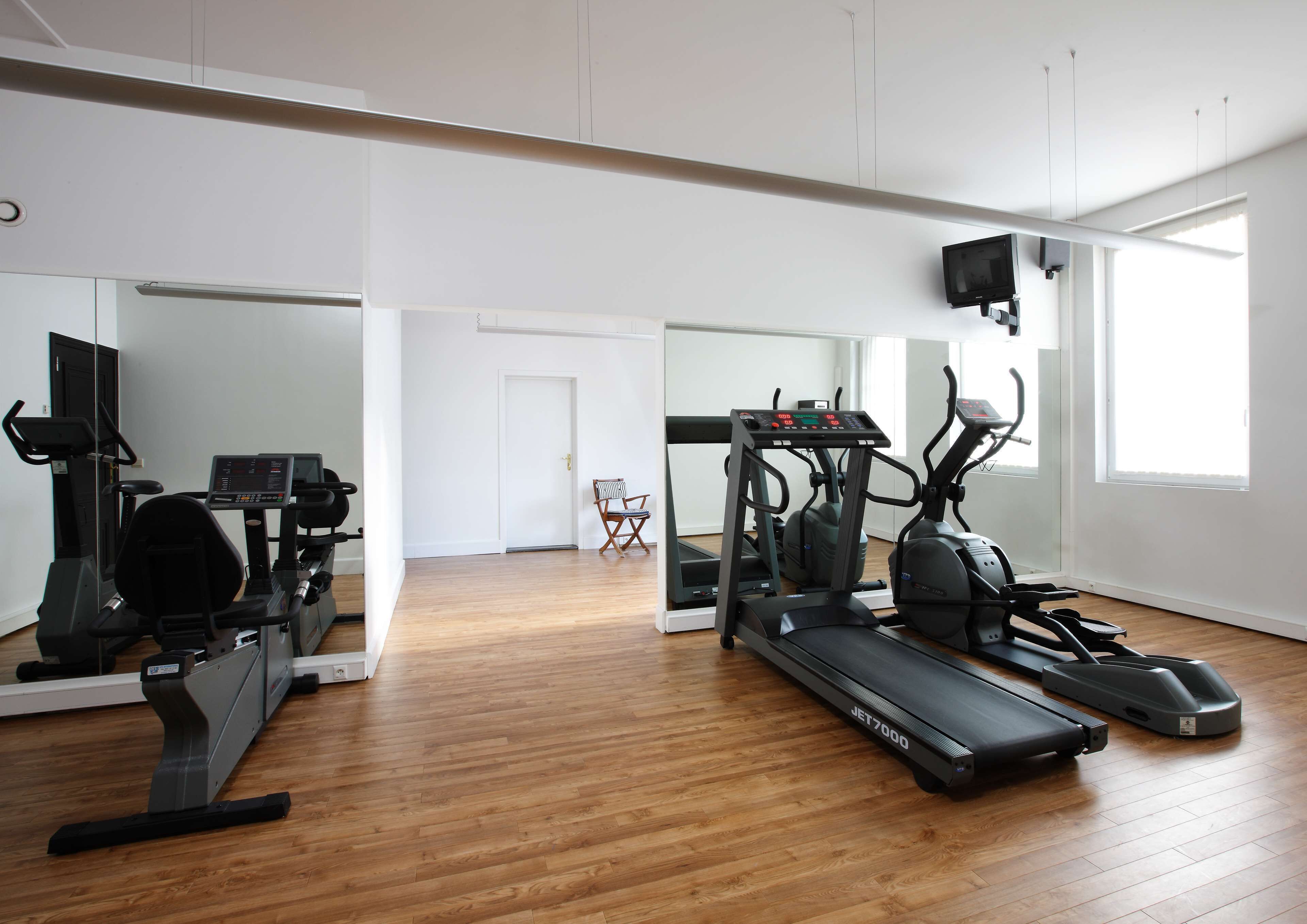 Un gimnasio con equipamiento de ejercicio, suelo de madera y ventanas amplias.