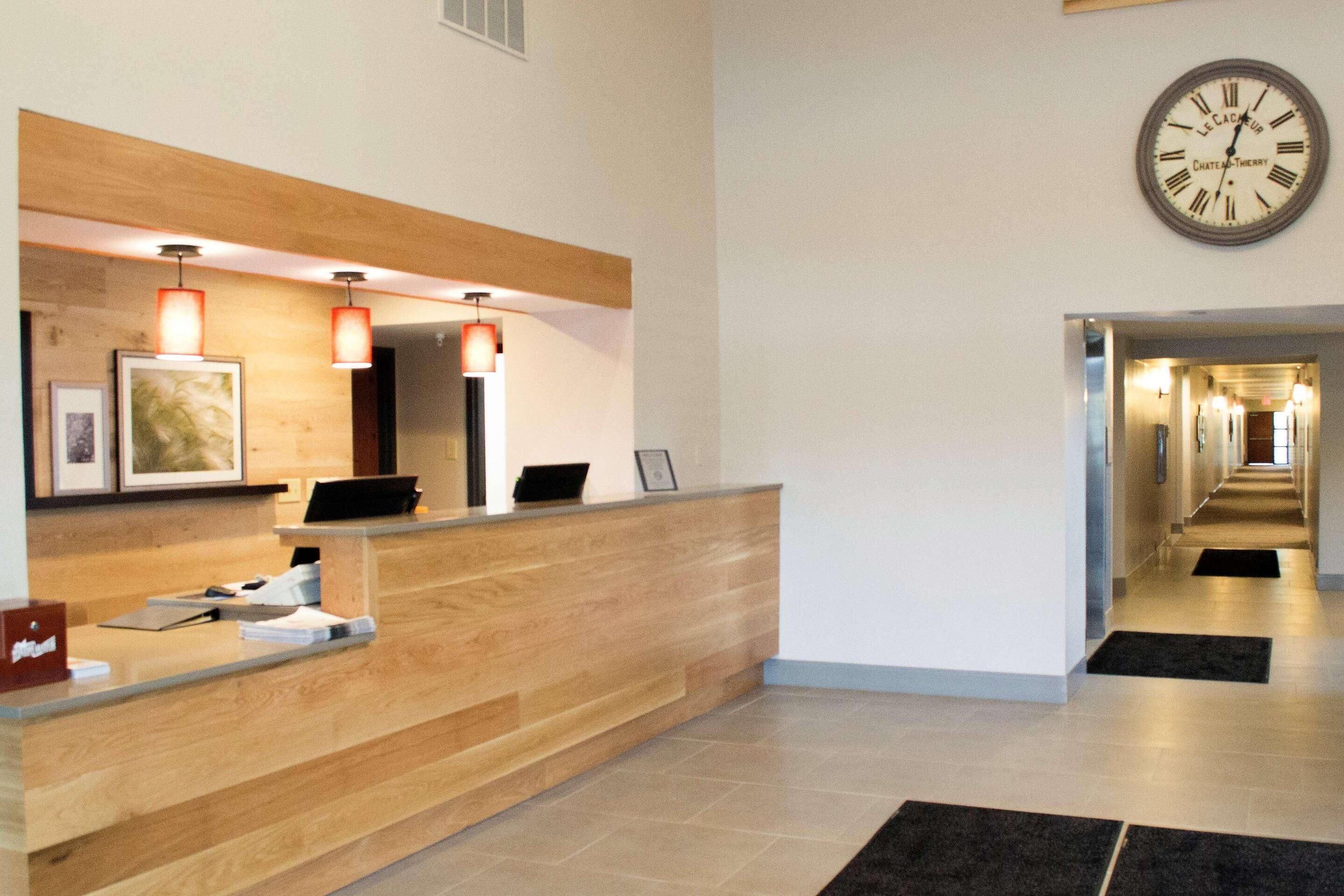 A hotel reception area with a wooden reception desk, a wall-mounted clock, and a hallway leading to other rooms.