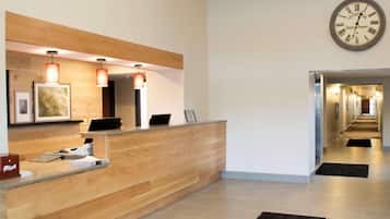A hotel reception area with a wooden reception desk, a wall-mounted clock, and a hallway leading to other rooms.