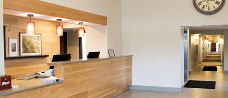 Zona de recepción de un hotel con un mostrador de madera, un reloj en la pared y un pasillo que conduce a otras habitaciones.