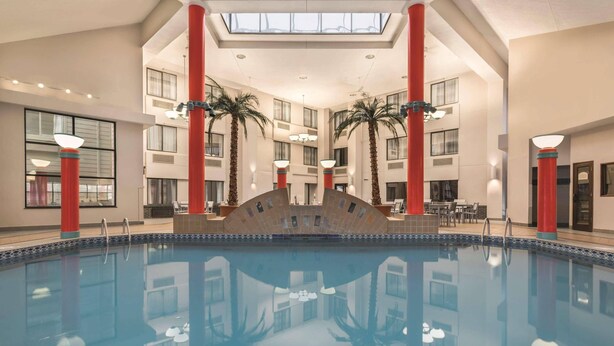A large indoor swimming pool with red pillars, a central fountain, and a high ceiling with skylights. - Country Inn & Suites by Radisson Erie (Erie)