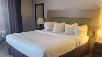 A large bed with white linens, a headboard, and a bedside lamp.