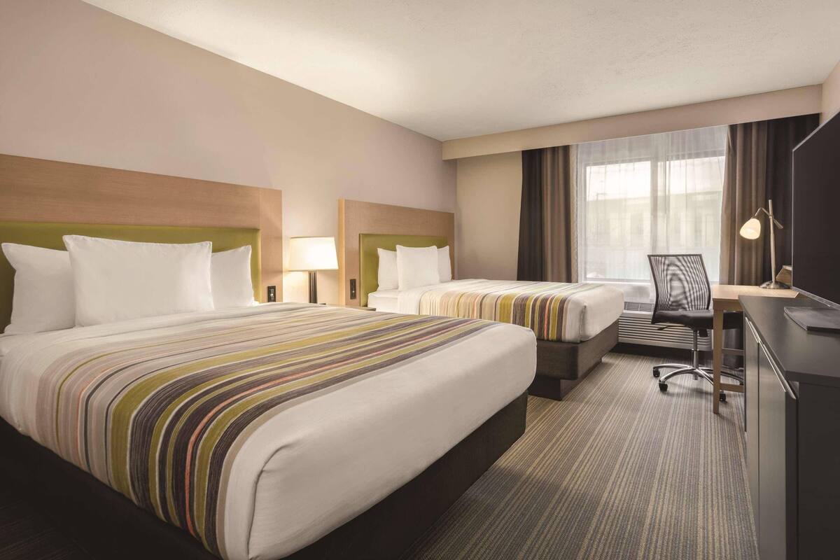 A hotel room with two beds, a desk, a chair, and a large window with curtains.