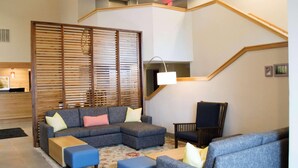 A modern living room with a sectional sofa, ottomans, a wooden partition, a chair, and a lamp. - Country Inn & Suites by Radisson Erie (Erie)