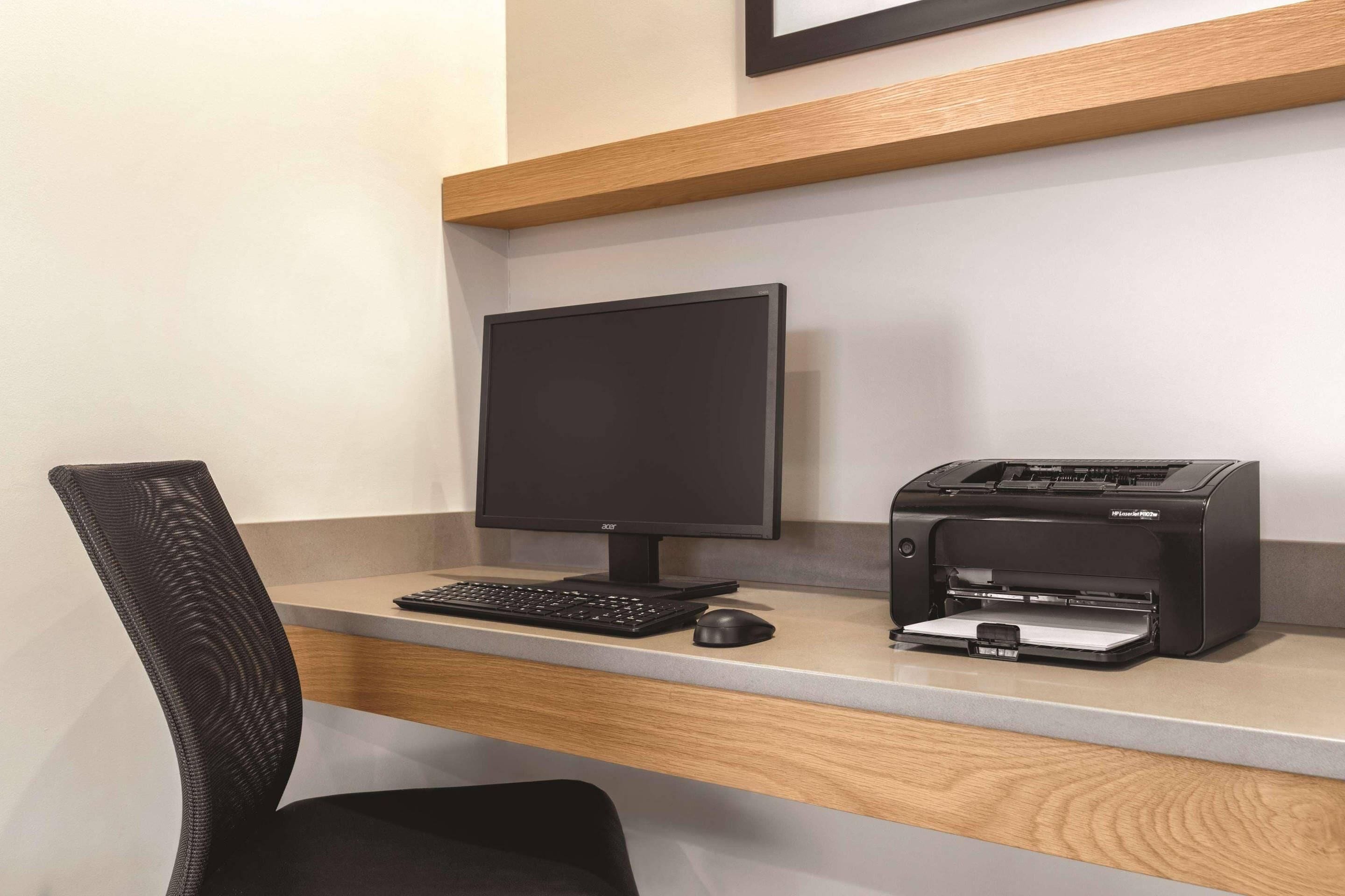 Un espacio de trabajo con monitor de computadora, teclado, ratón e impresora sobre un escritorio.
