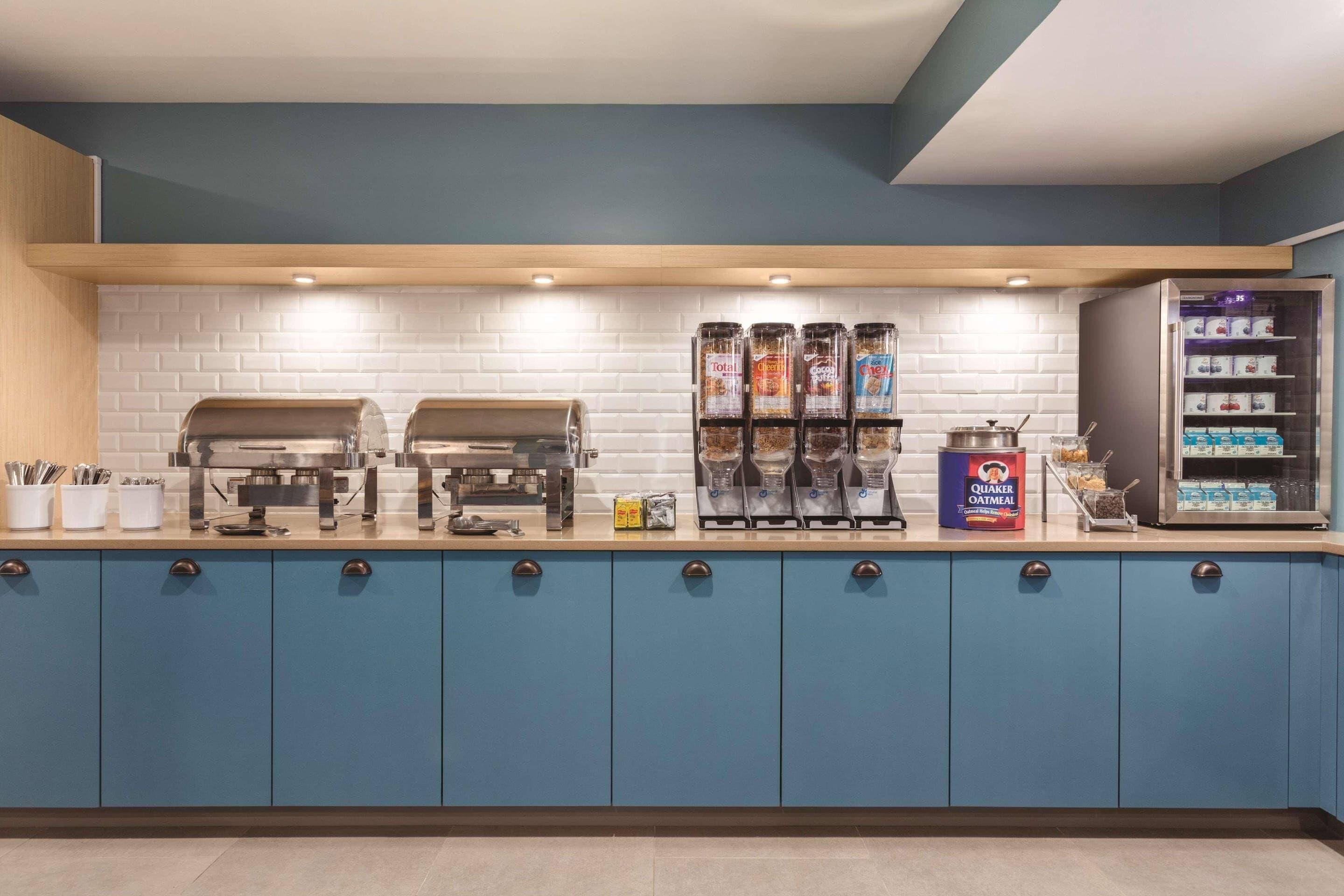 A modern kitchen with blue cabinets, a coffee station, and a refrigerator stocked with beverages.